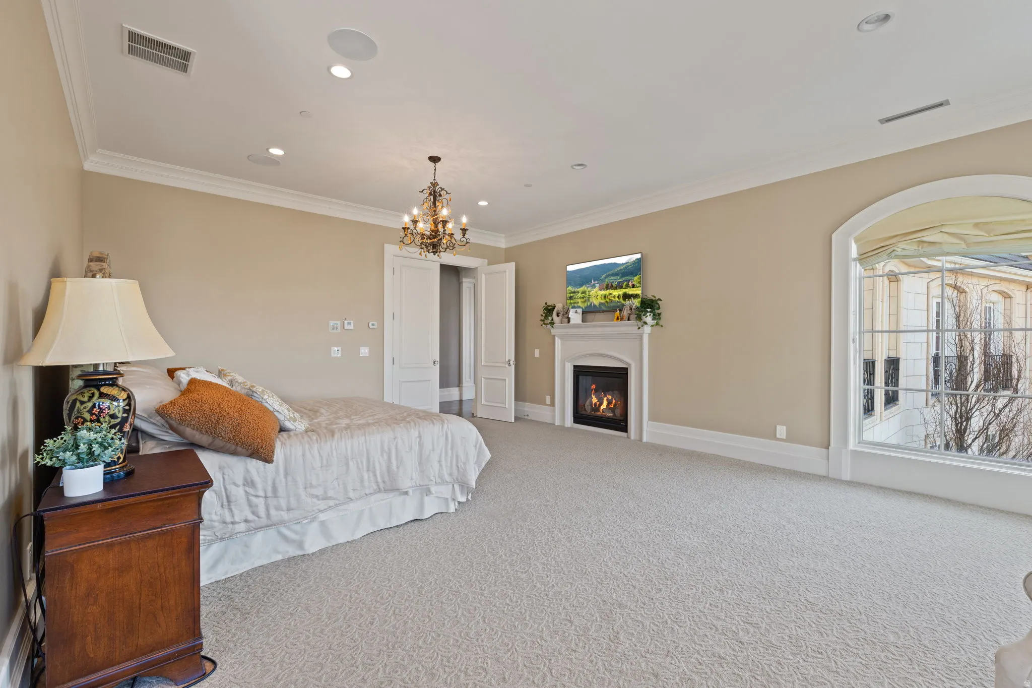 Carpeted bedroom featuring a glass covered fireplace, crown molding, and suspended lighting