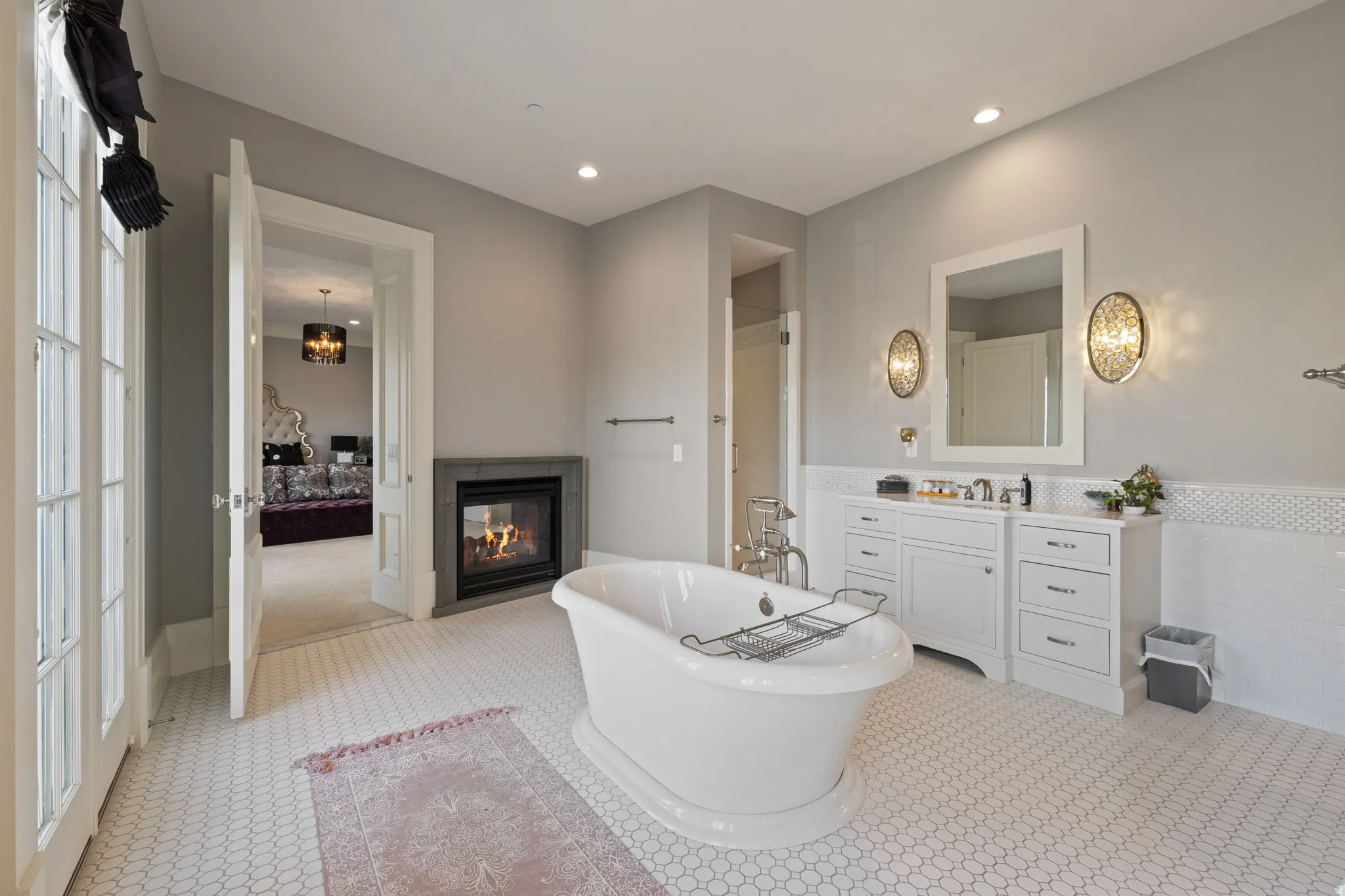 Ensuite bathroom featuring a multi sided fireplace, a soaking tub, vanity, recessed lighting, and wainscoting