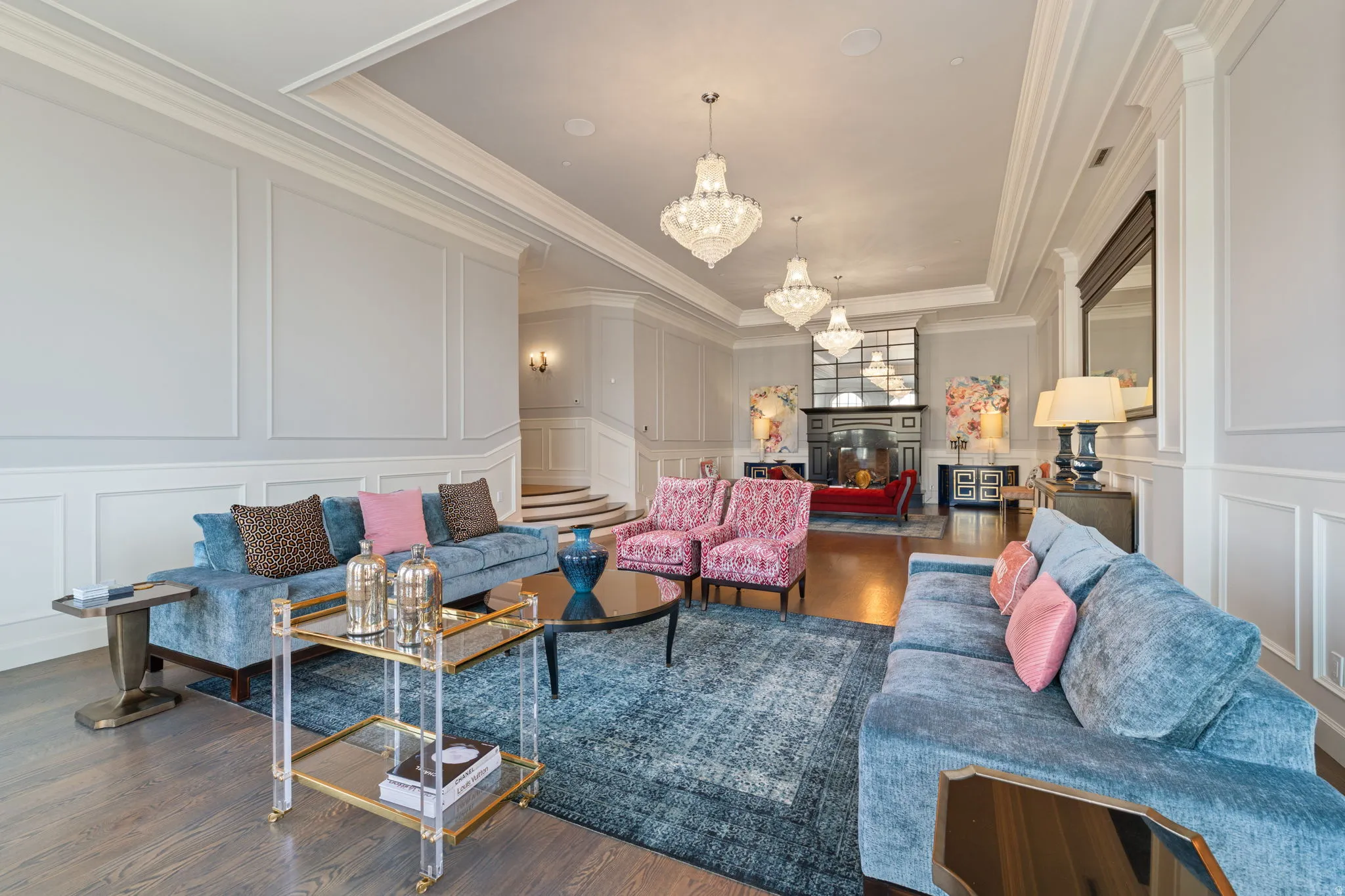 Living room with a decorative wall, a glass covered fireplace, dark wood-style flooring, suspended lighting, and crown molding