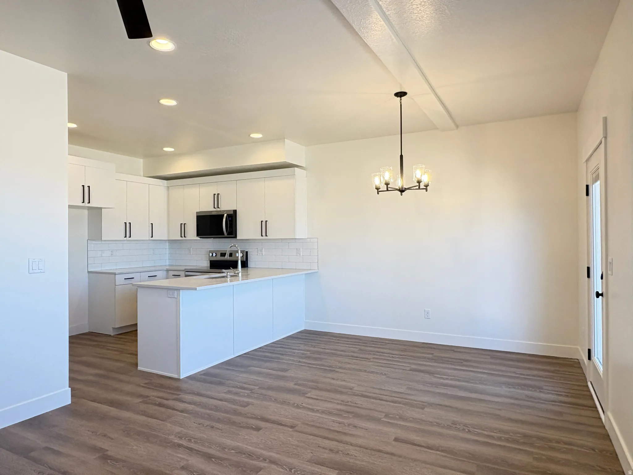 Kitchen featuring white cabinetry, a peninsula, tasteful backsplash, stainless steel appliances, and dark wood finished floors