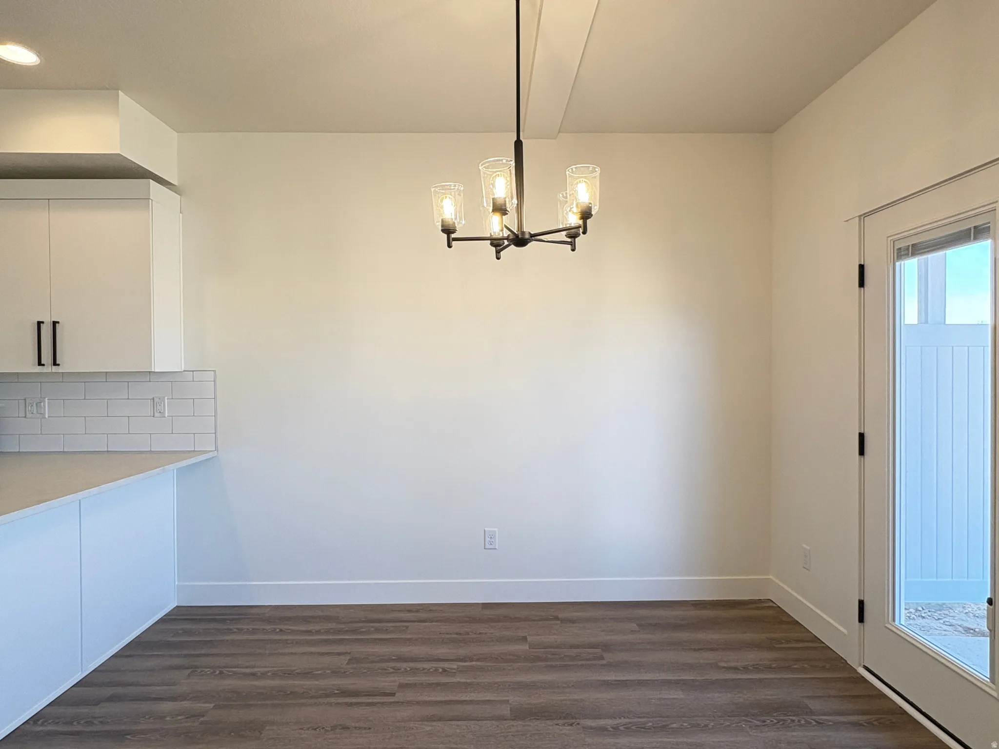 Unfurnished dining area with dark wood-style flooring and suspended lighting