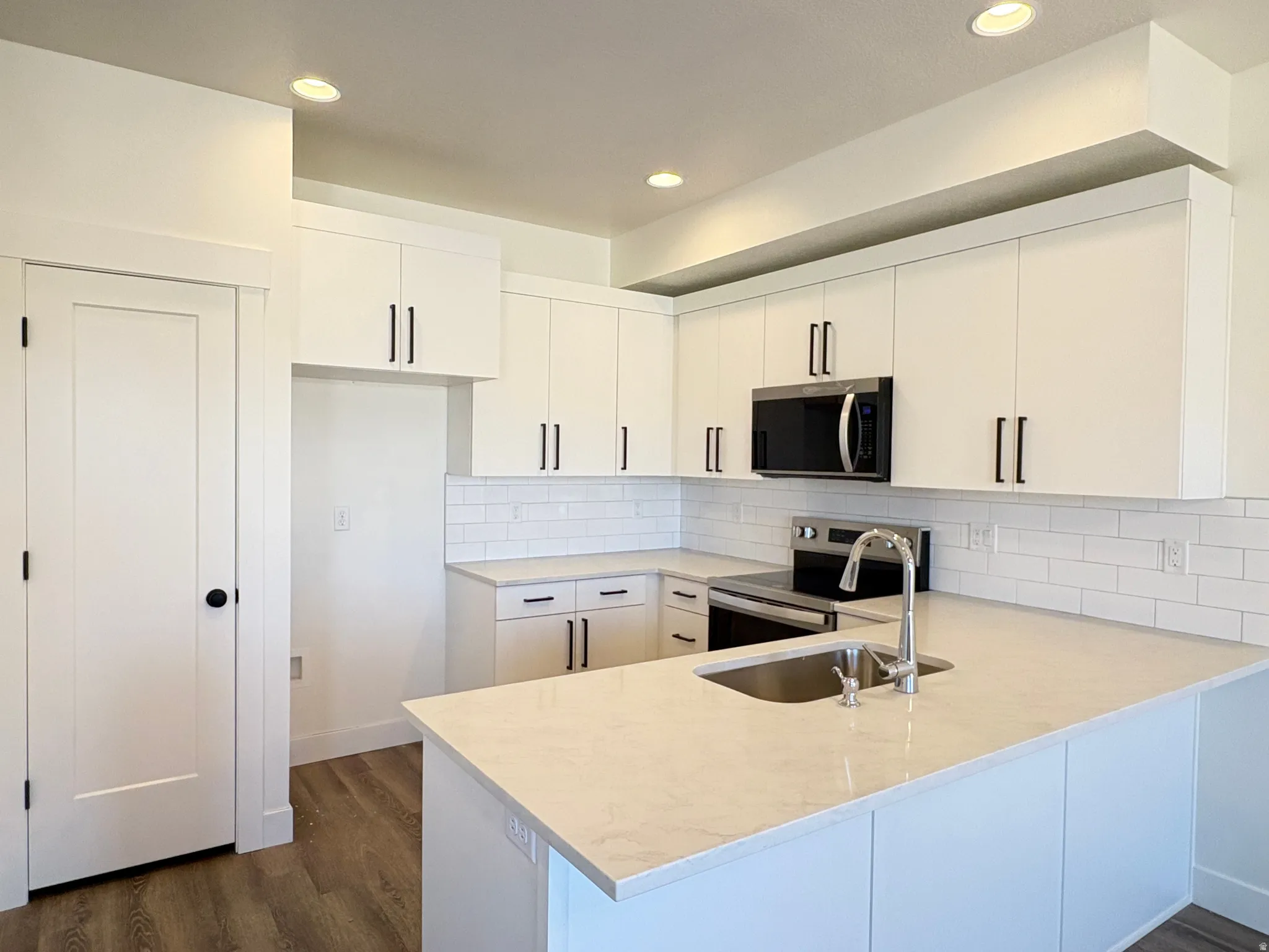 Kitchen with a peninsula, stainless steel appliances, backsplash, dark wood-type flooring, and white cabinetry
