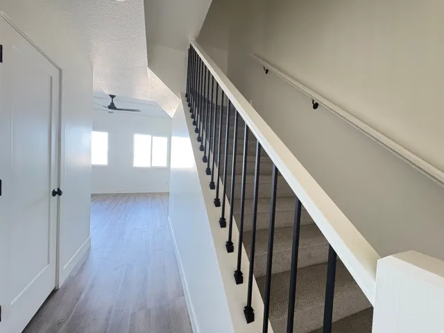 Stairs with a ceiling fan, wood finished floors, and a textured ceiling