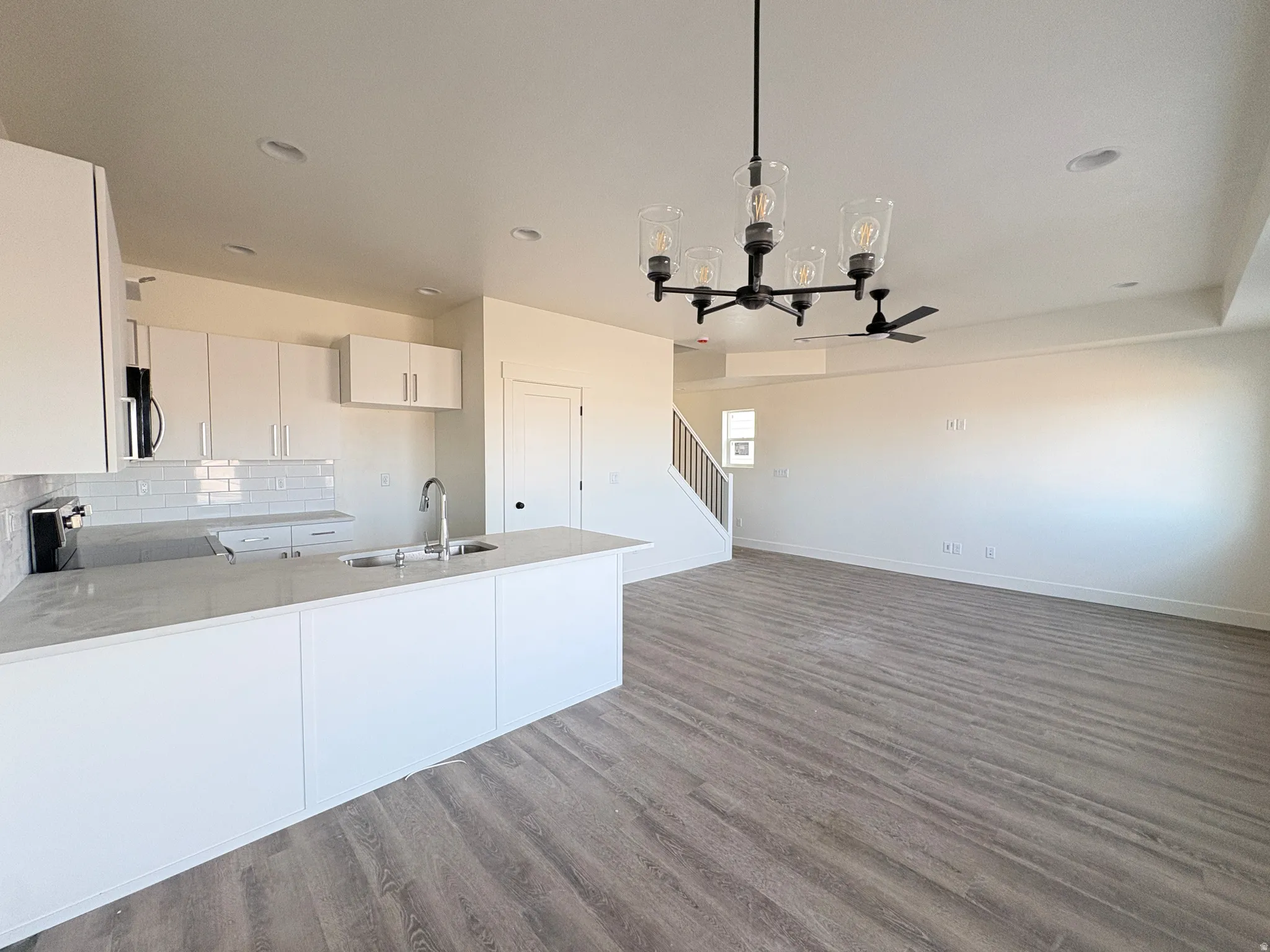 Kitchen with suspended lighting, white cabinets, a peninsula, dark wood-style flooring, and stainless steel appliances