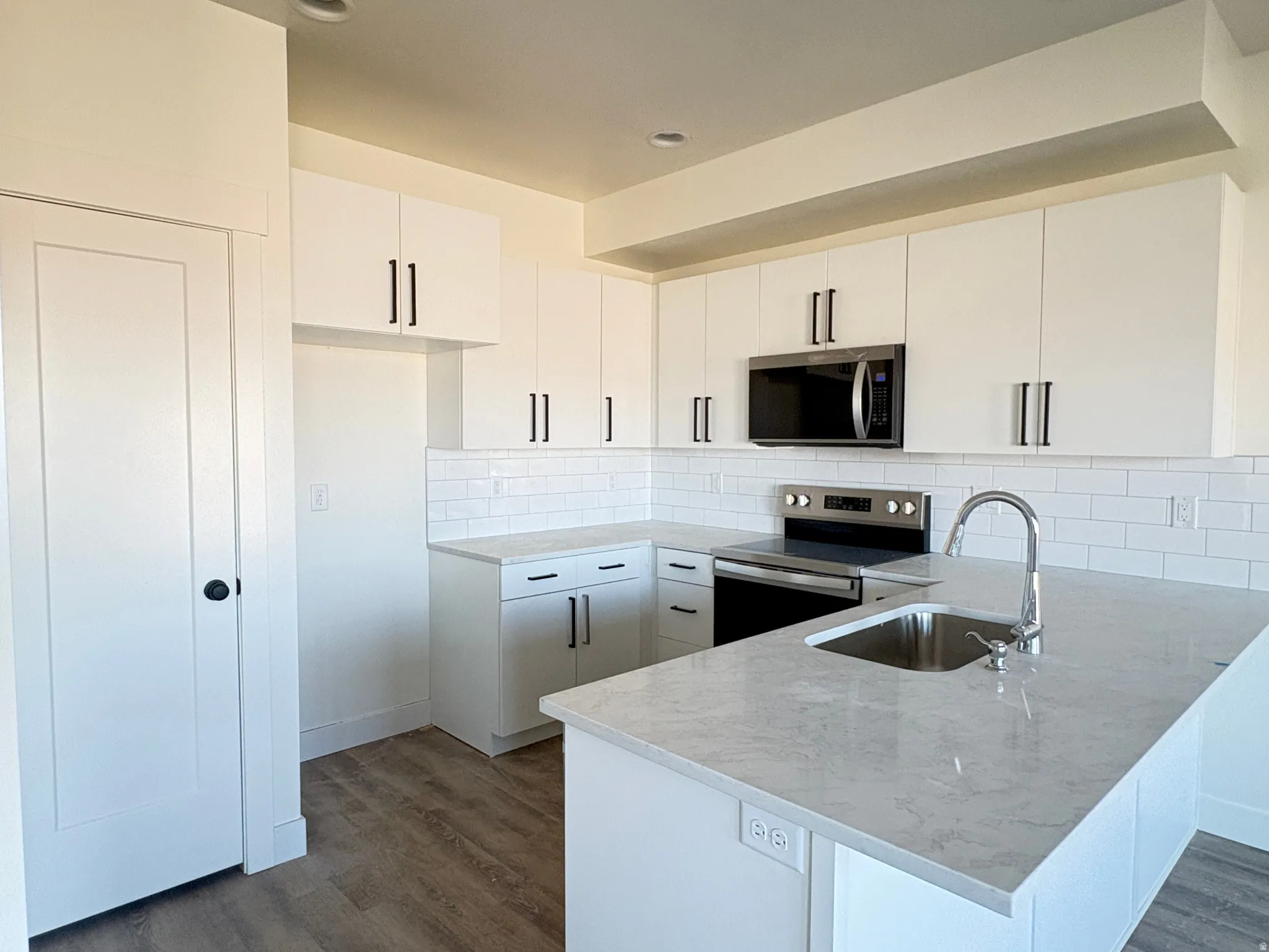 Kitchen with stainless steel appliances, a peninsula, dark wood-type flooring, and backsplash