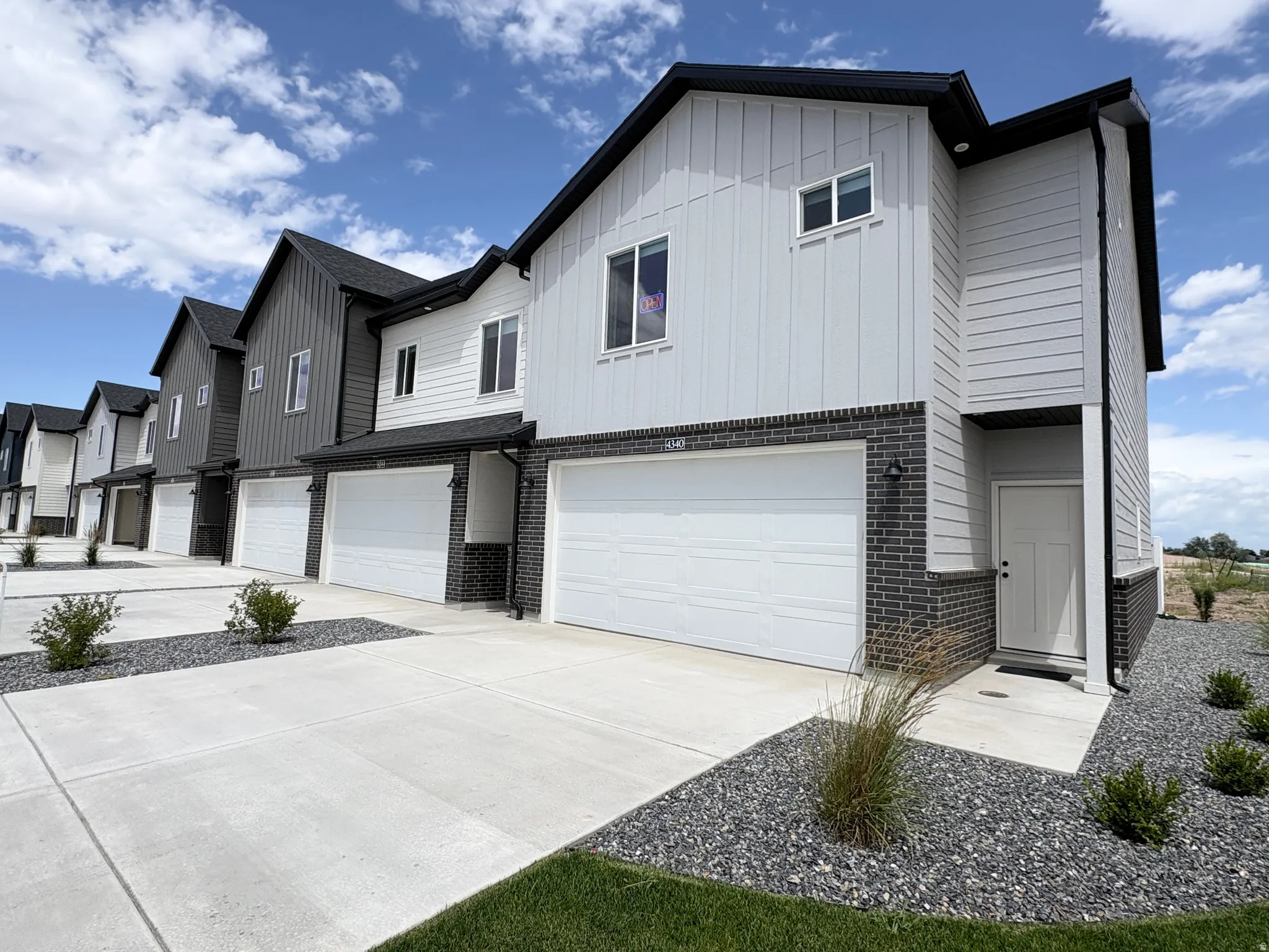 Contemporary townhome exterior featuring light gray siding, dark gray brick accents, and a black shingle roof