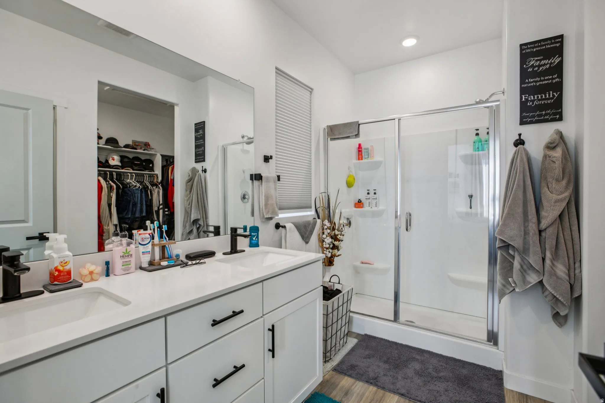 Bathroom with double vanity, a walk in closet, a shower stall, and dark wood-type flooring