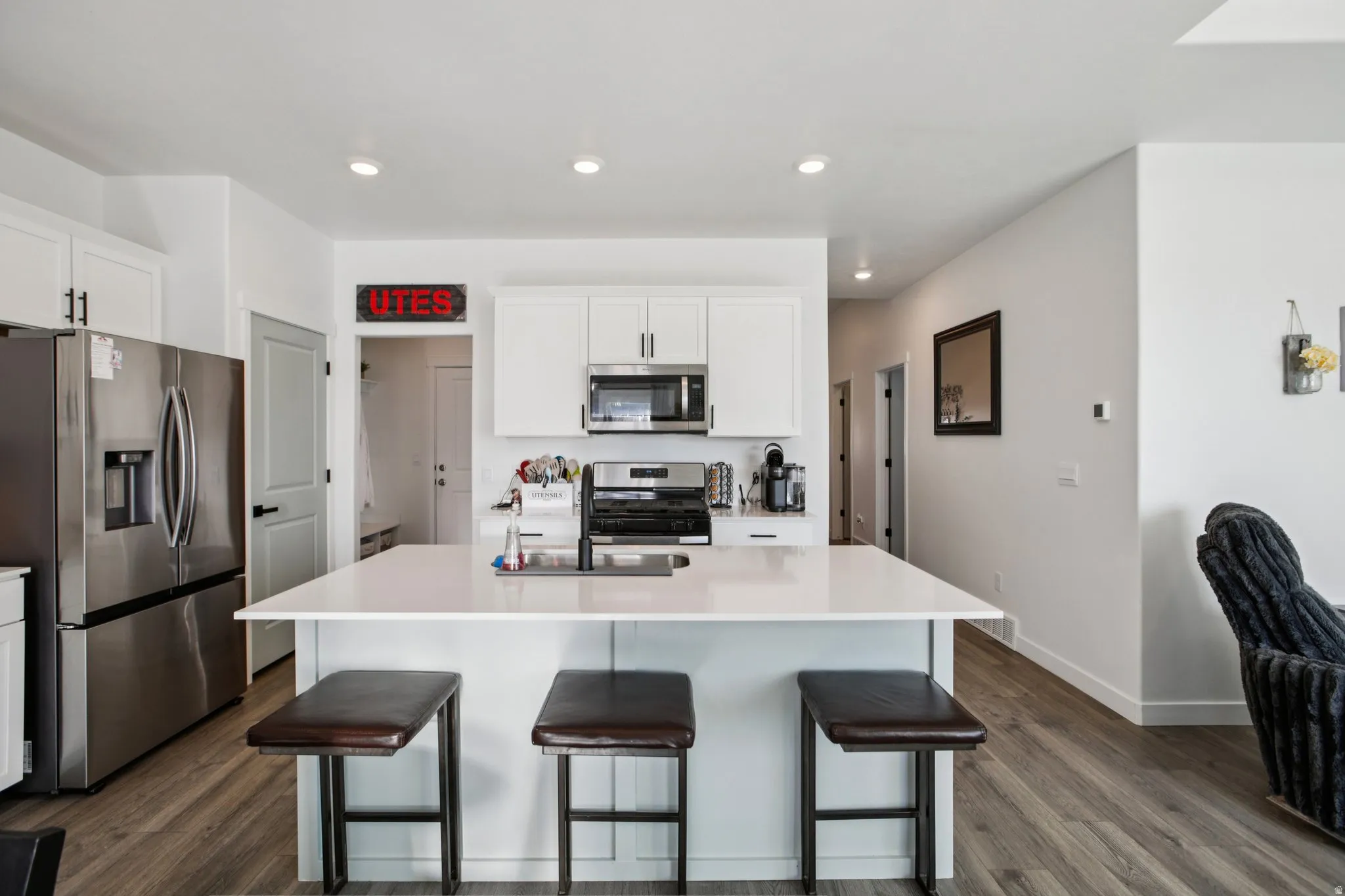 Kitchen featuring stainless steel appliances, white cabinets, an island with sink, a breakfast bar area, and recessed lighting