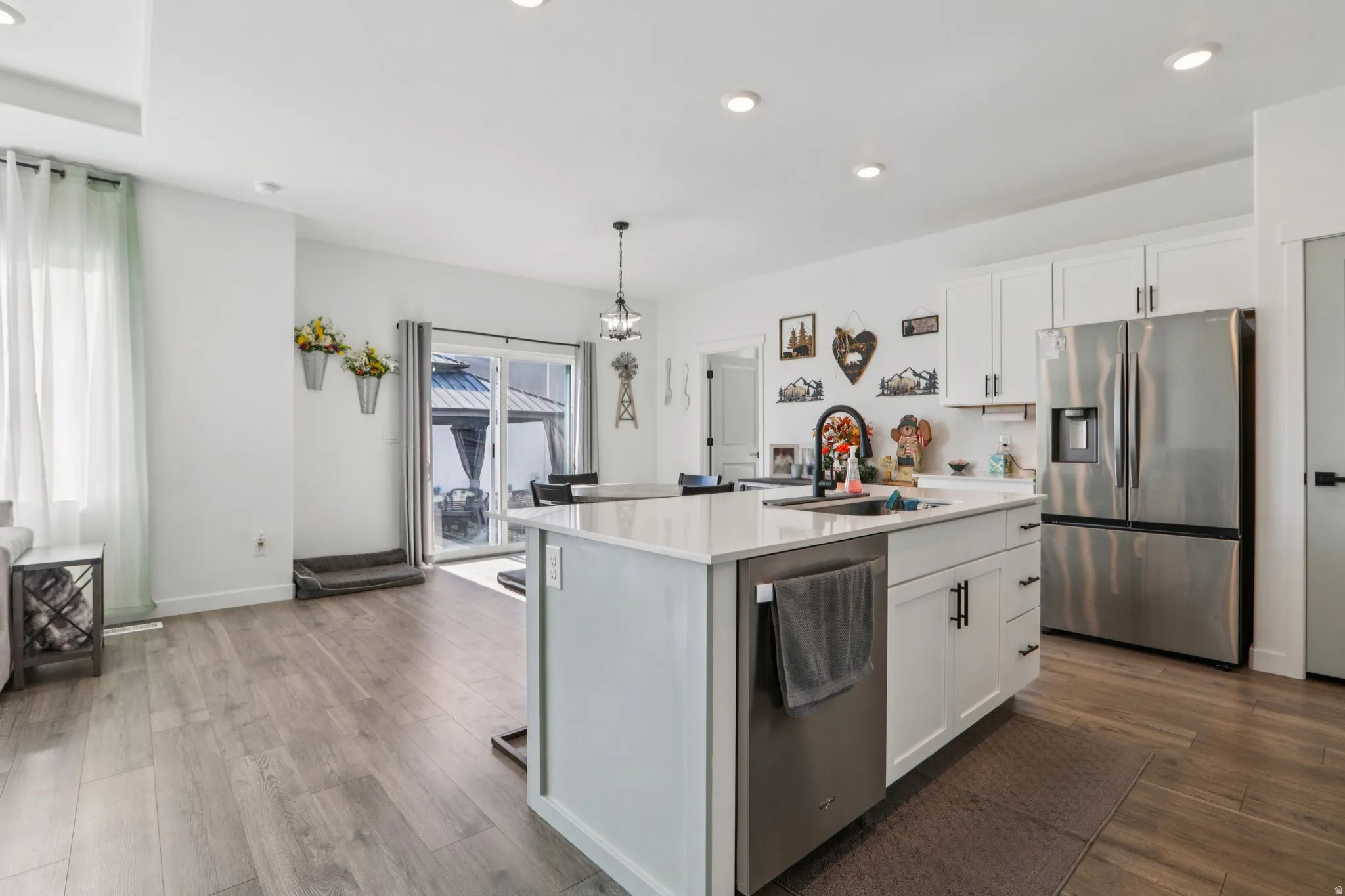 Kitchen with stainless steel appliances, a center island with sink, white cabinets, dark wood-type flooring, and hanging light fixtures