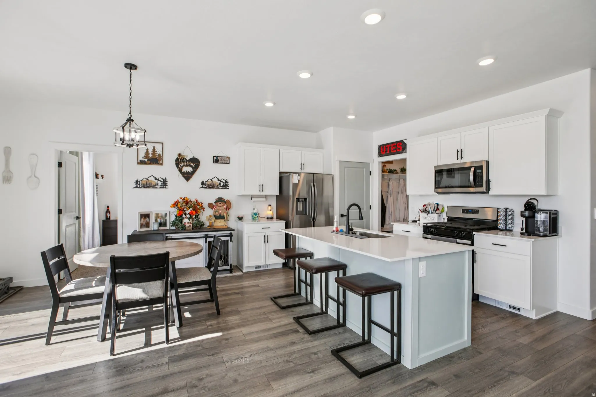 Kitchen featuring a kitchen bar, stainless steel appliances, an island with sink, white cabinetry, and dark wood finished floors