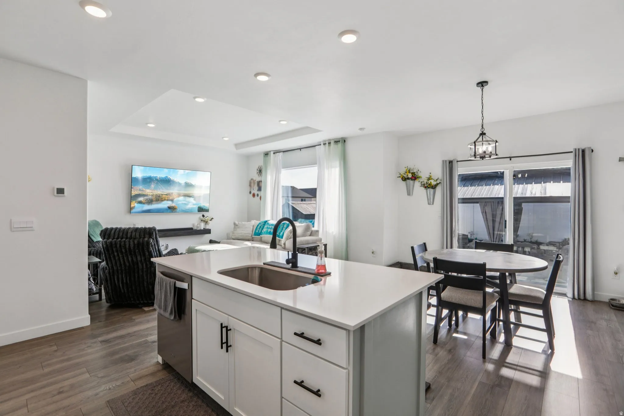 Kitchen with decorative light fixtures, dark wood finished floors, a raised ceiling, white cabinets, and a kitchen island with sink