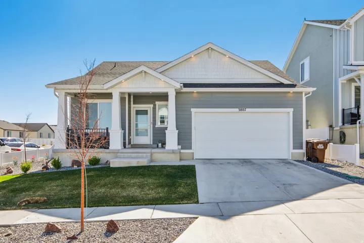 View of front of house featuring a front lawn, covered porch, a garage, driveway, and a shingled roof