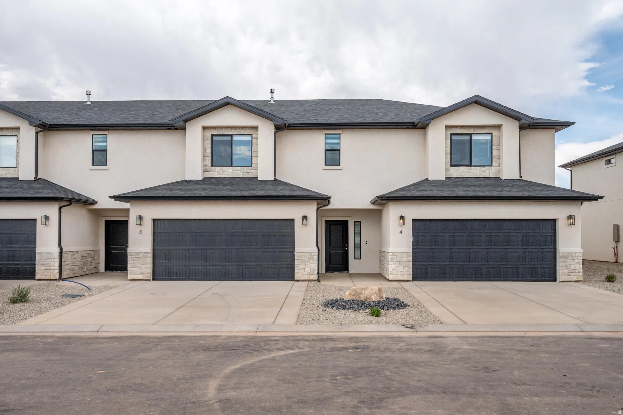 View of front facade with stucco siding, stone siding, concrete driveway, and an attached garage
