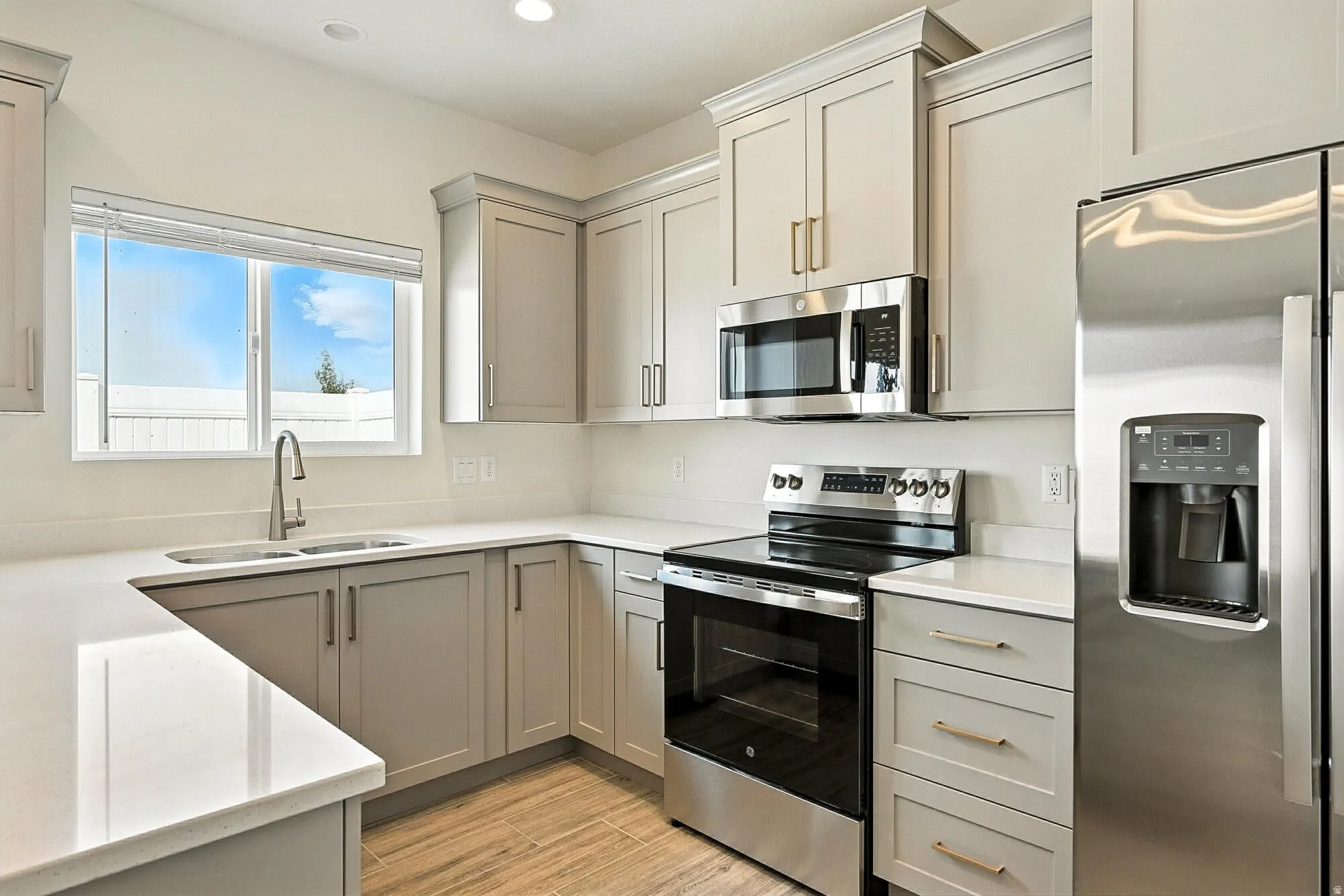 Kitchen with stainless steel appliances, gray cabinets, light wood-type flooring, recessed lighting, and light stone countertops