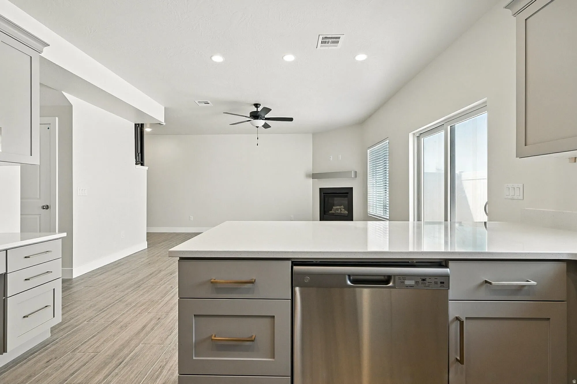 Kitchen with stainless steel dishwasher, a ceiling fan, light stone counters, a glass covered fireplace, and a peninsula
