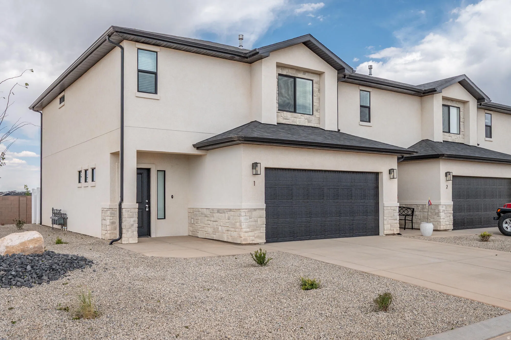 View of front facade featuring stone siding, stucco siding, driveway, and a garage