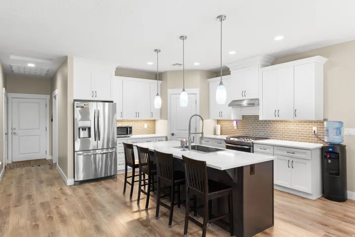 Dual tone kitchen featuring a kitchen breakfast bar, stainless steel appliances, an island with sink, hanging light fixtures, and two tone cabinetry