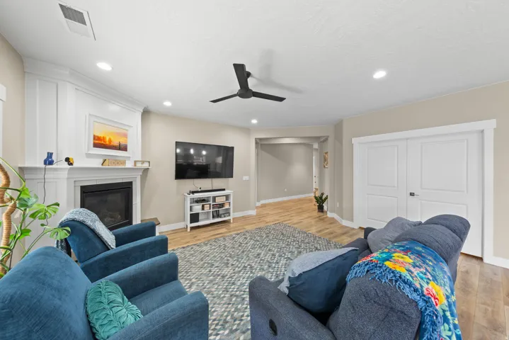 Living room featuring light wood-type flooring, a ceiling fan, a glass covered fireplace, and recessed lighting