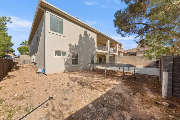 Rear view of property with a fenced backyard, a trampoline, a patio, stucco siding, and a balcony
