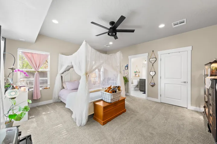 Bedroom with light colored carpet, a ceiling fan, and ensuite bathroom