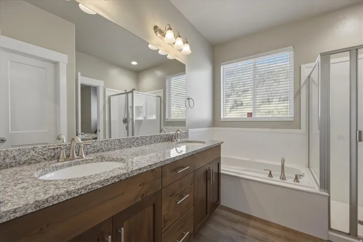 Full bath featuring a stall shower, double vanity, a garden tub, and light wood-type flooring