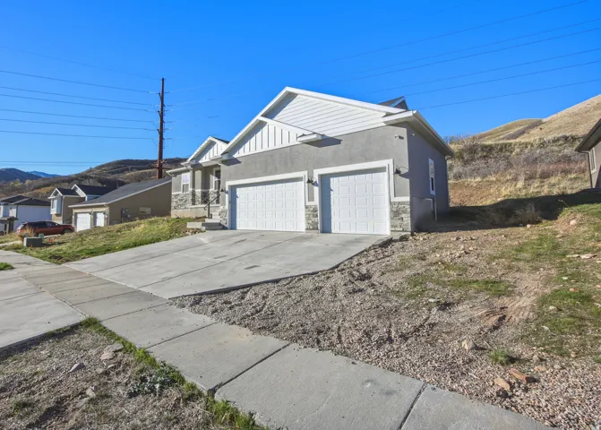 View of side of home with an attached garage, concrete driveway, stone siding, a mountain view, and stucco siding