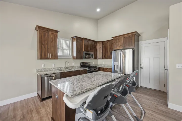 Kitchen featuring dark wood finish cabinetry, light stone countertops, stainless steel appliances, a kitchen island, and a kitchen bar
