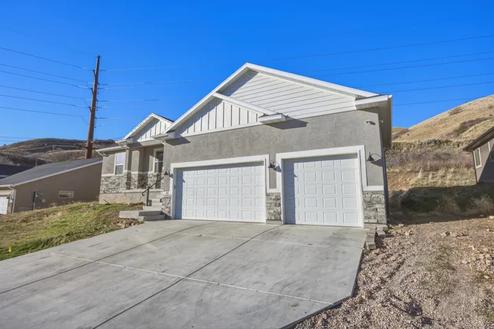 View of front facade featuring an attached garage, concrete driveway, stone siding, board and batten siding, and stucco siding