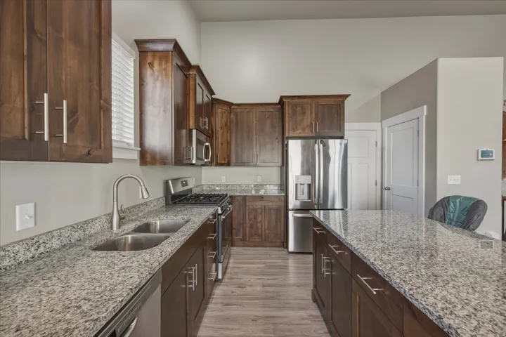 Kitchen with stainless steel appliances, dark wood finish cabinets, light stone counters, and light wood-style flooring