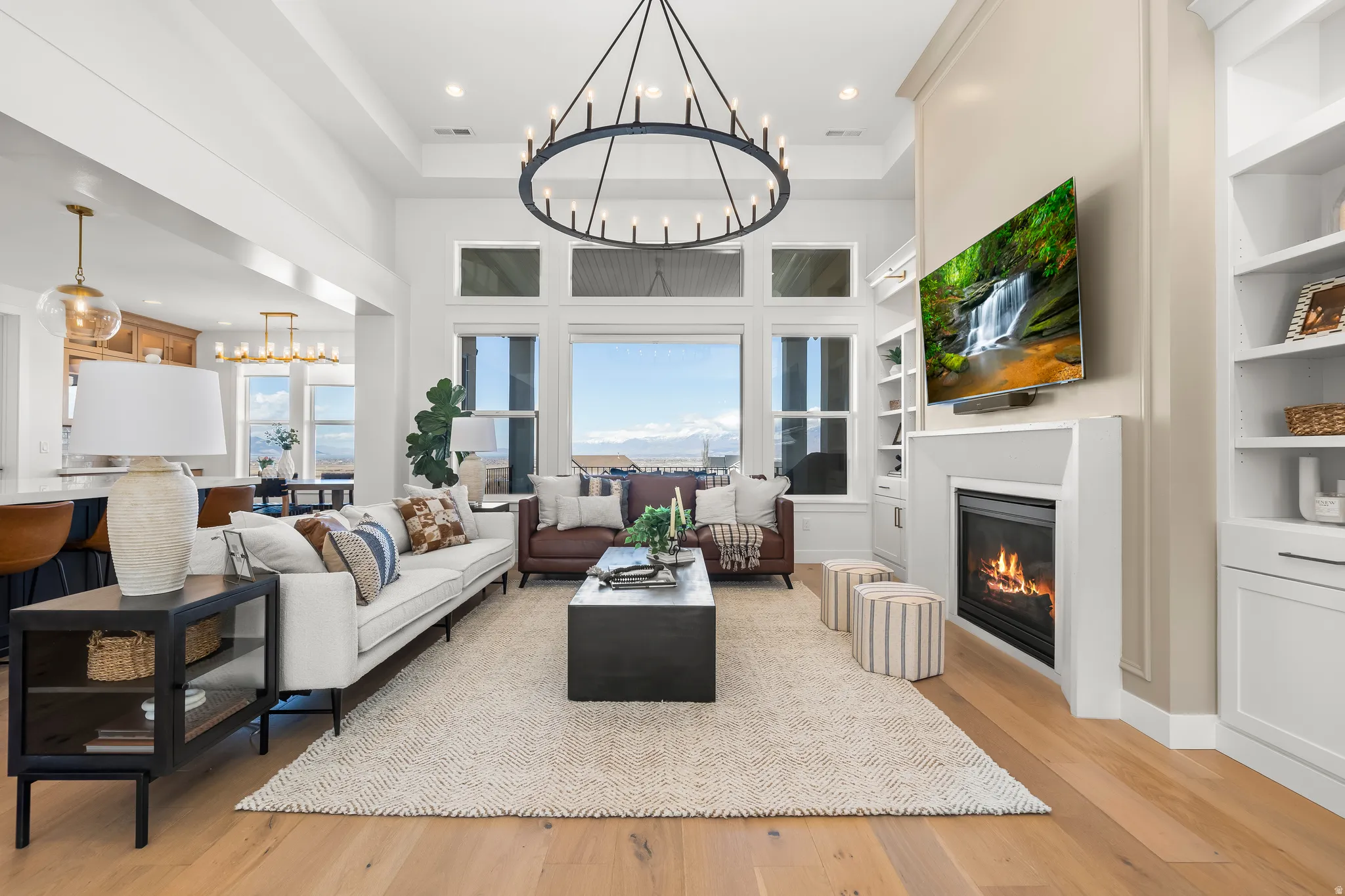 Living room with a chandelier, plenty of natural light, light wood-style flooring, a glass covered fireplace, and a high tray ceiling