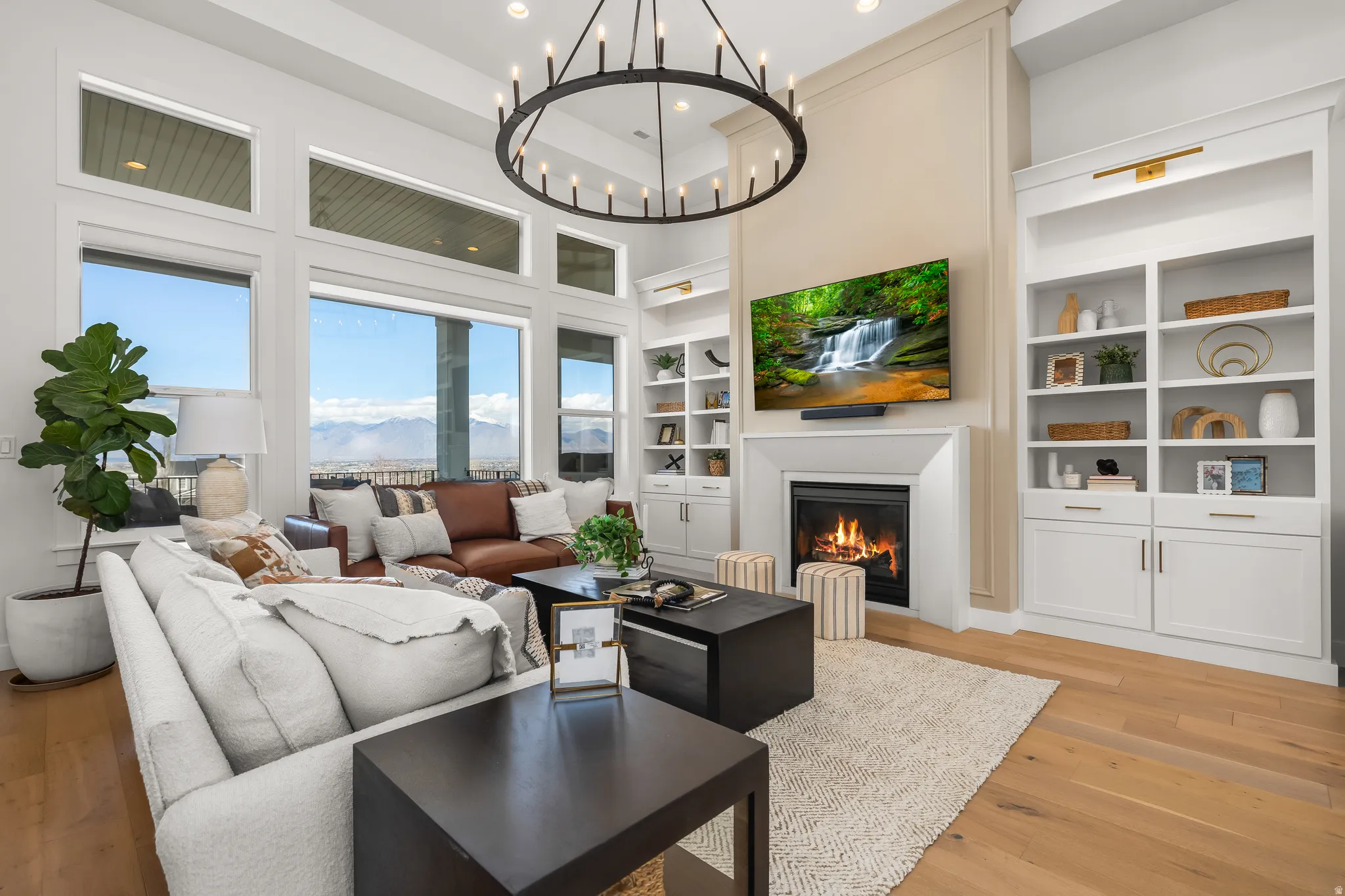 Living area with built in shelves, a glass covered fireplace, light wood-style floors, a chandelier, and a high ceiling