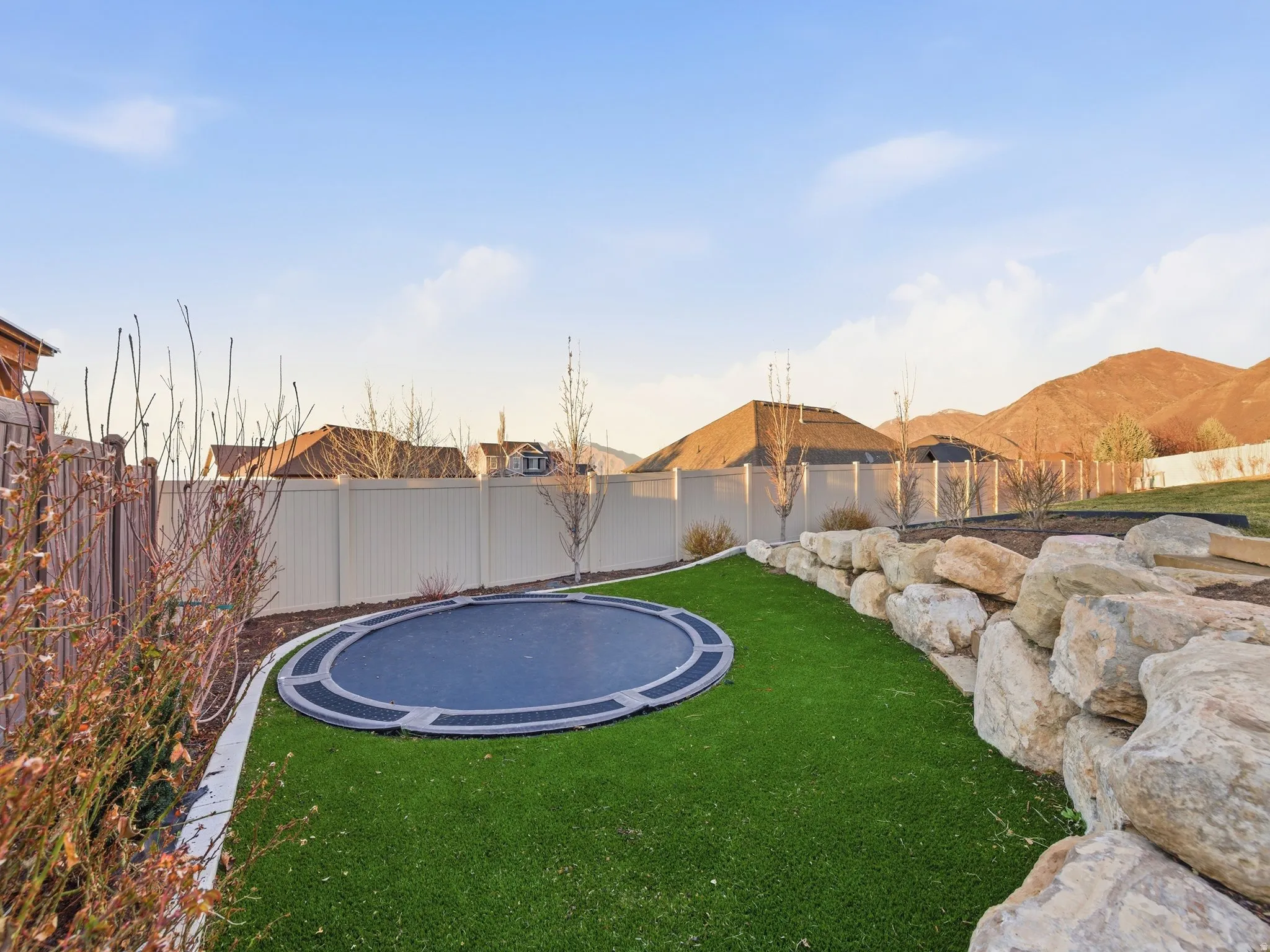 Fenced backyard featuring a trampoline and a patio area