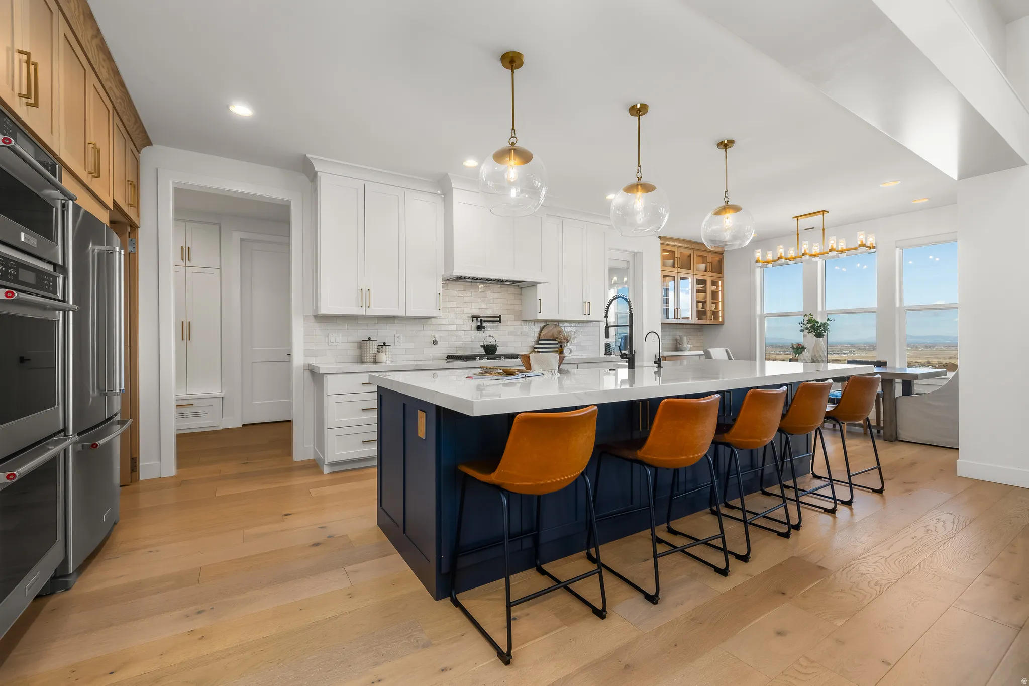 Two tone kitchen with two tone cabinetry, light wood-type flooring, a breakfast bar area, a large island with sink, and light stone counters