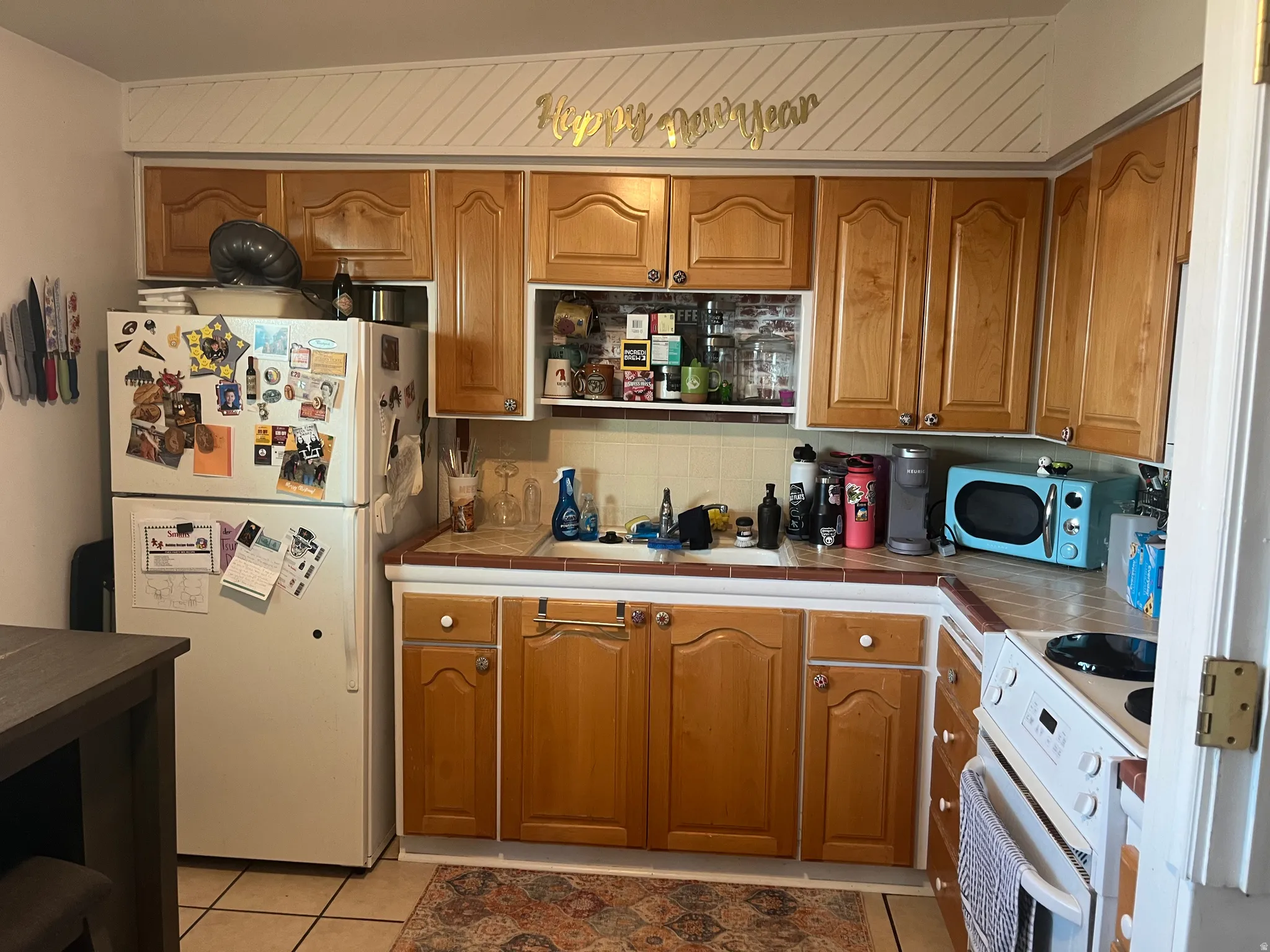 Kitchen with tile countertops, white appliances, decorative backsplash, and wood finish cabinetry