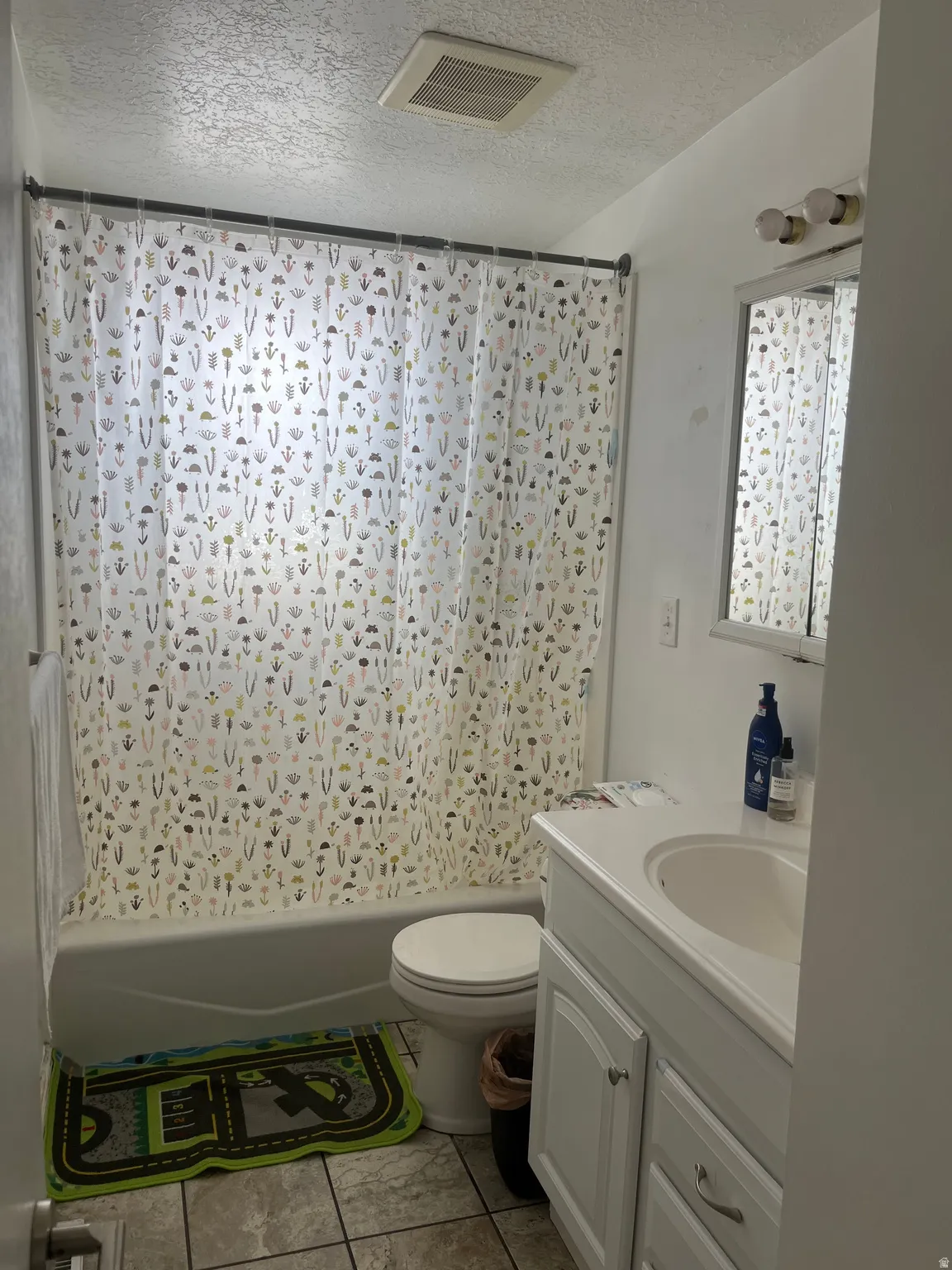 Full bath with a textured ceiling, vanity, shower / tub combo with curtain, and light tile patterned floors