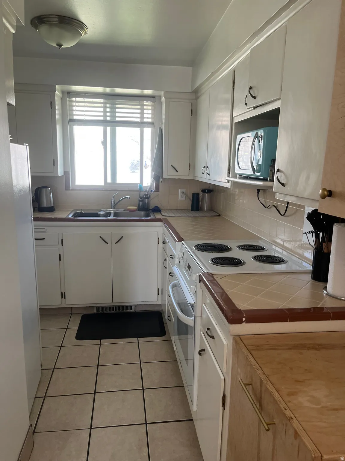 Kitchen with white appliances, light tile patterned floors, white cabinetry, tile counters, and decorative backsplash
