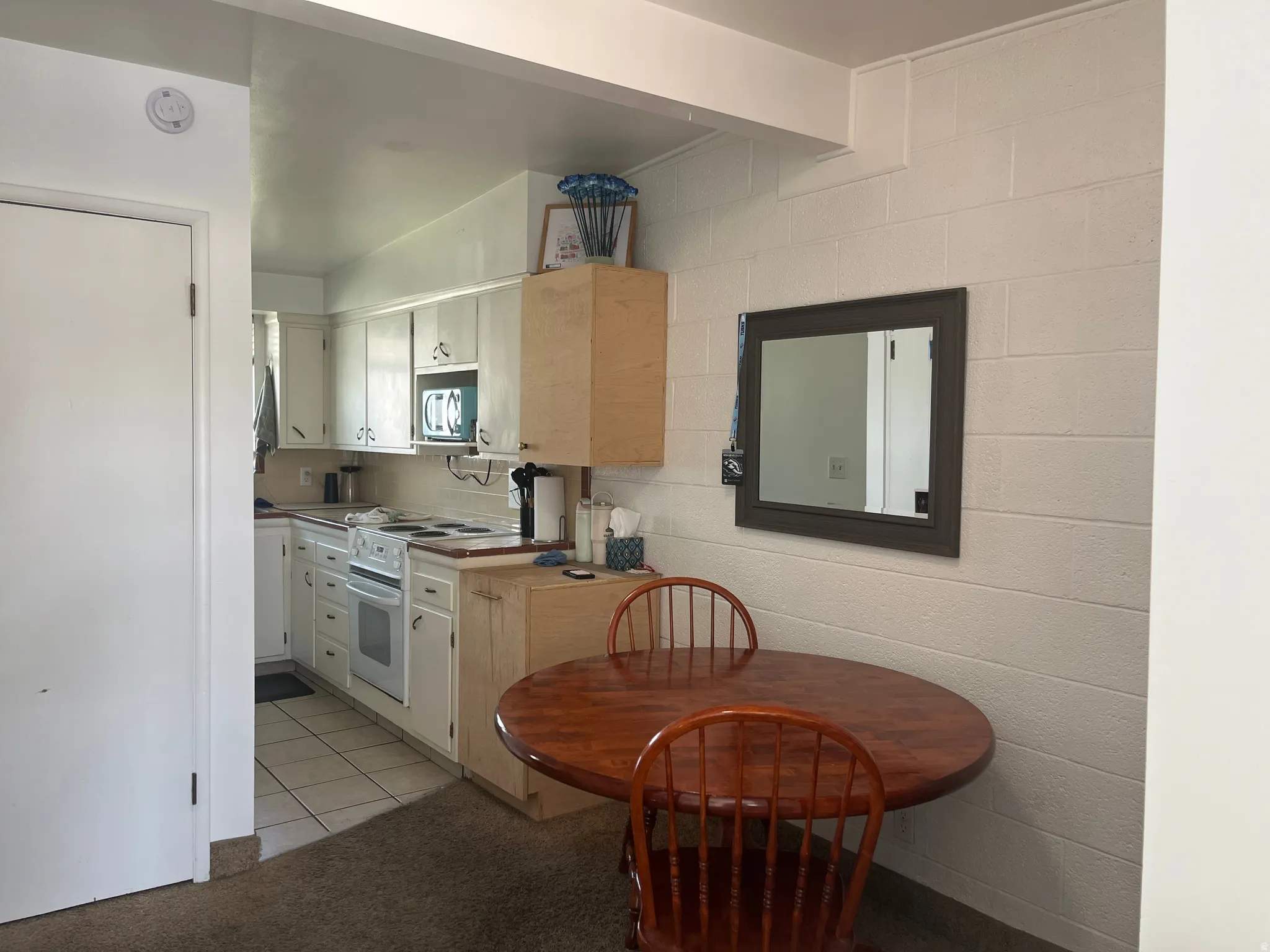 Kitchen with electric stove, light countertops, light colored carpet, light tile patterned floors, and white cabinetry