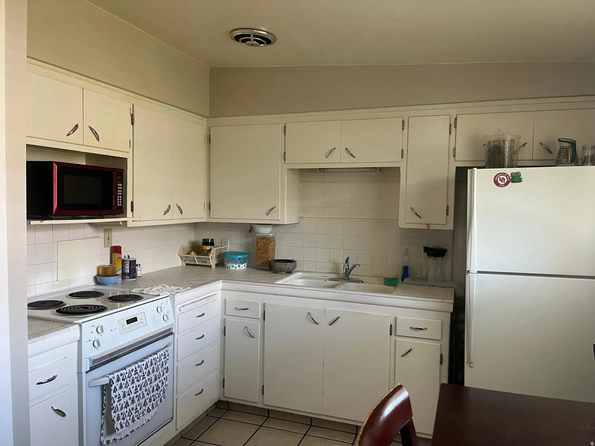 Kitchen with white appliances, light tile patterned flooring, white cabinetry, and decorative backsplash