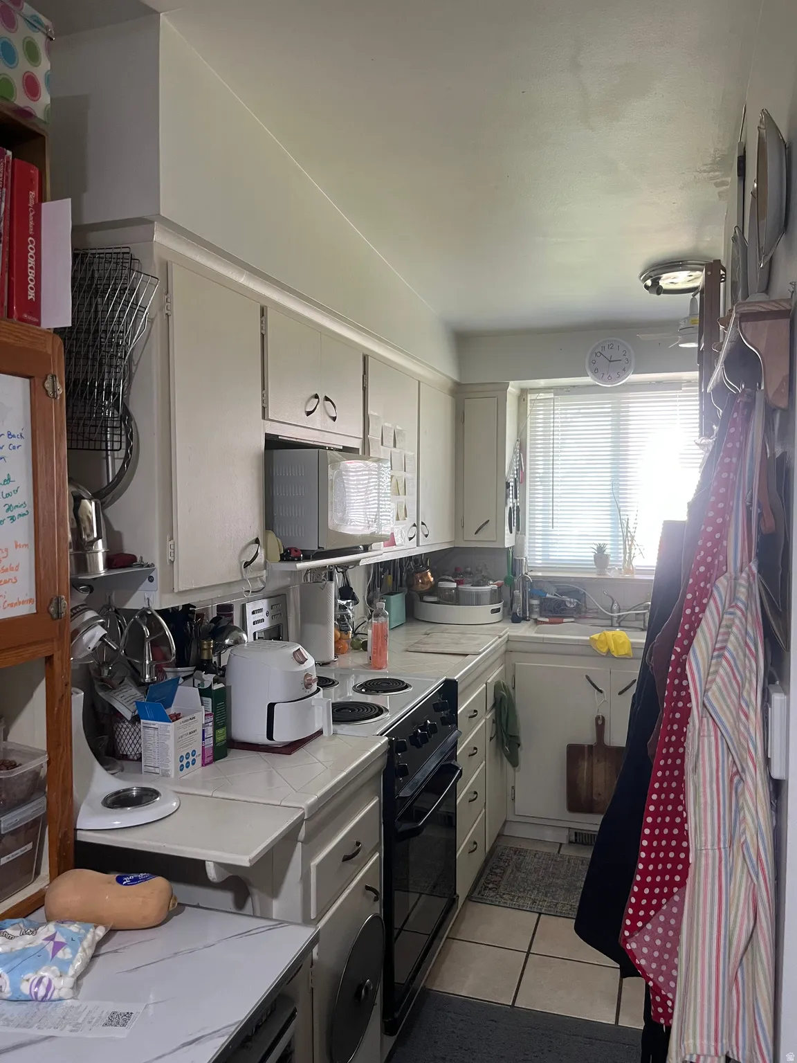 Kitchen with electric range, light tile patterned floors, white cabinets, and tile countertops