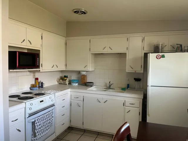 Kitchen with white appliances, light tile patterned flooring, white cabinetry, and decorative backsplash