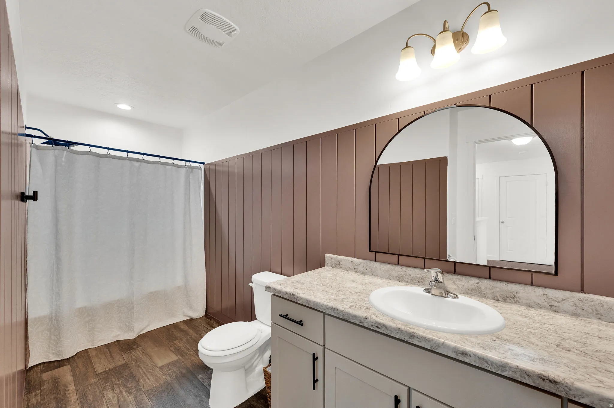 Full bath featuring vanity, dark wood-style floors, wooden walls, shower / bath combo with shower curtain, and wainscoting
