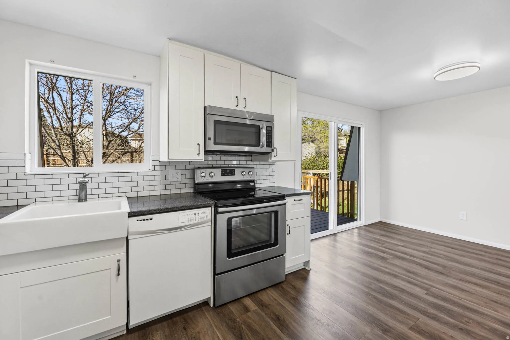 Kitchen with stainless steel appliances, white cabinetry, quartz counters, vinyl flooring, and decorative backsplash