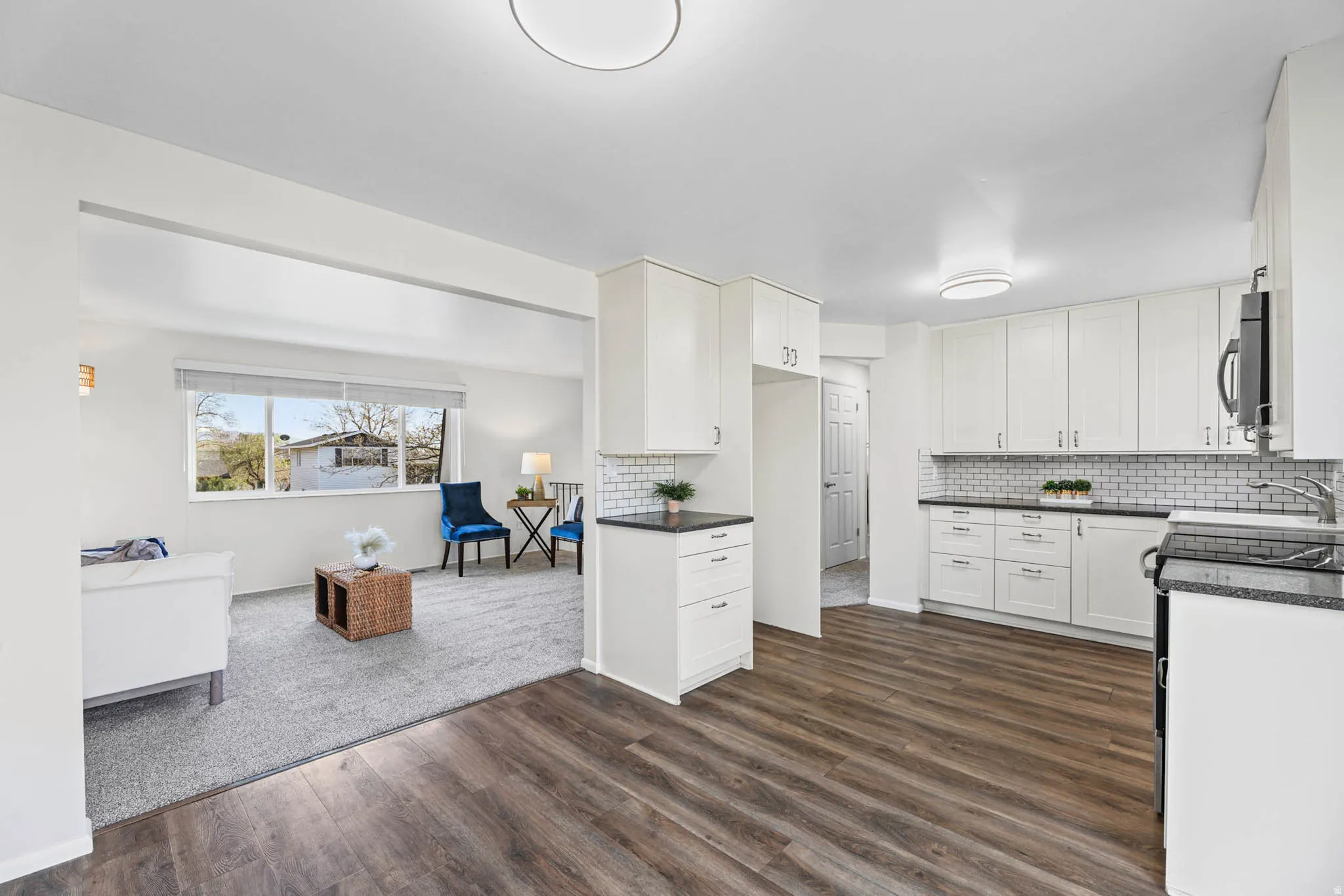 Kitchen with electric range, microwaave hood, vinyl floors, white cabinetry, quartz countertops and decorative backsplash