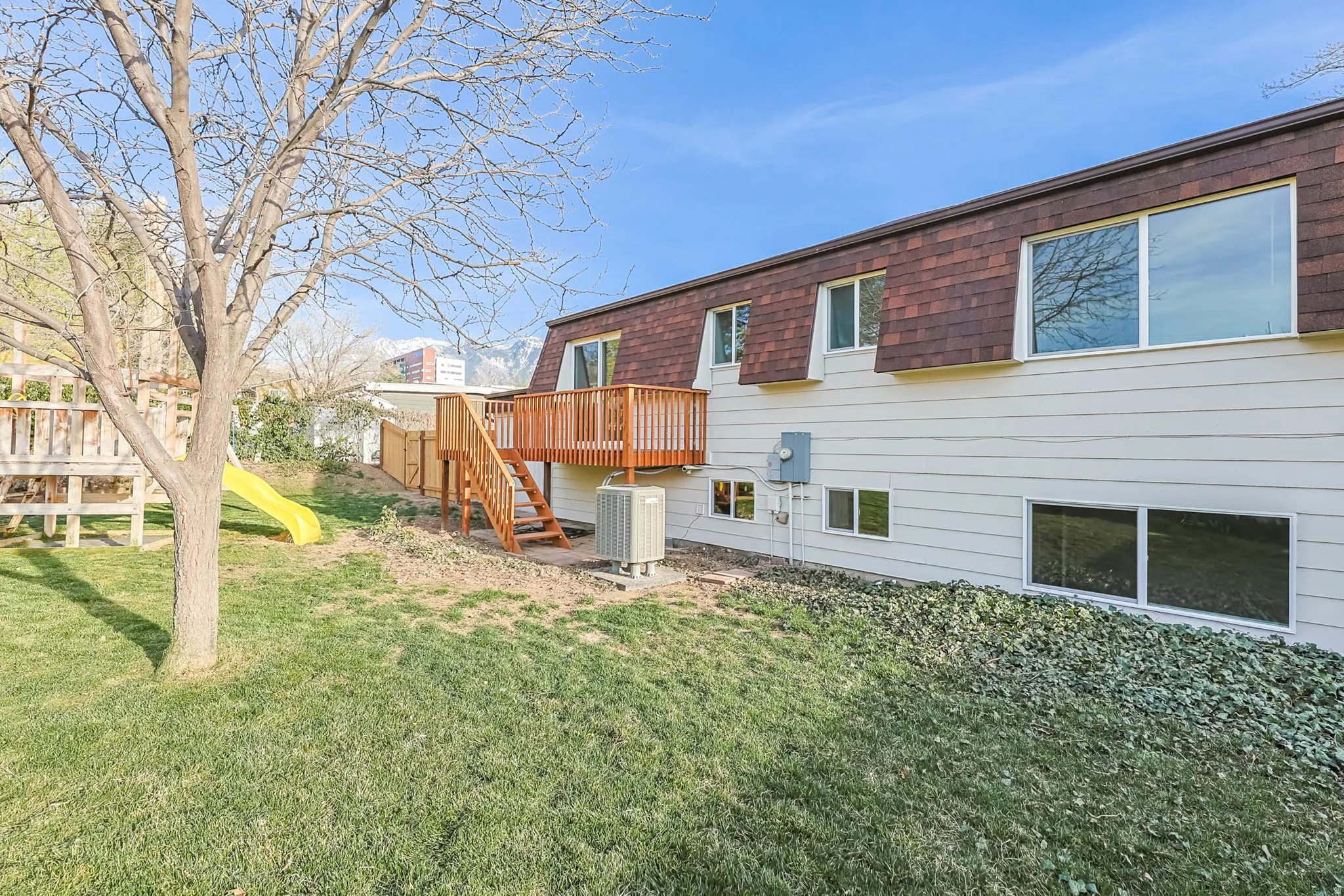 Back of house featuring a playground, a lawn, a deck, and mansard roof