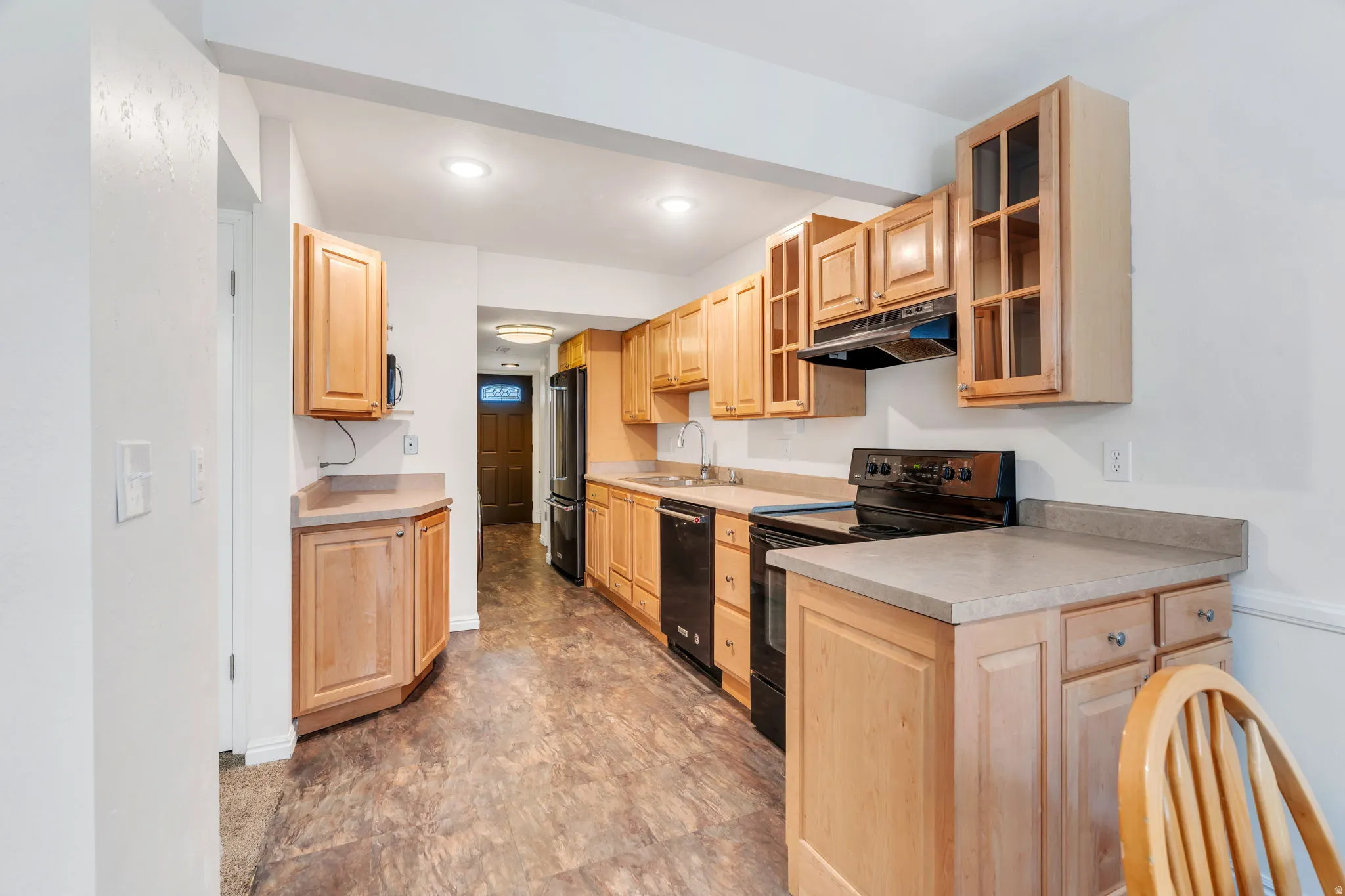 Kitchen with glass fronted cabinets, black appliances, light countertops, light wood finish cabinets, and recessed lighting