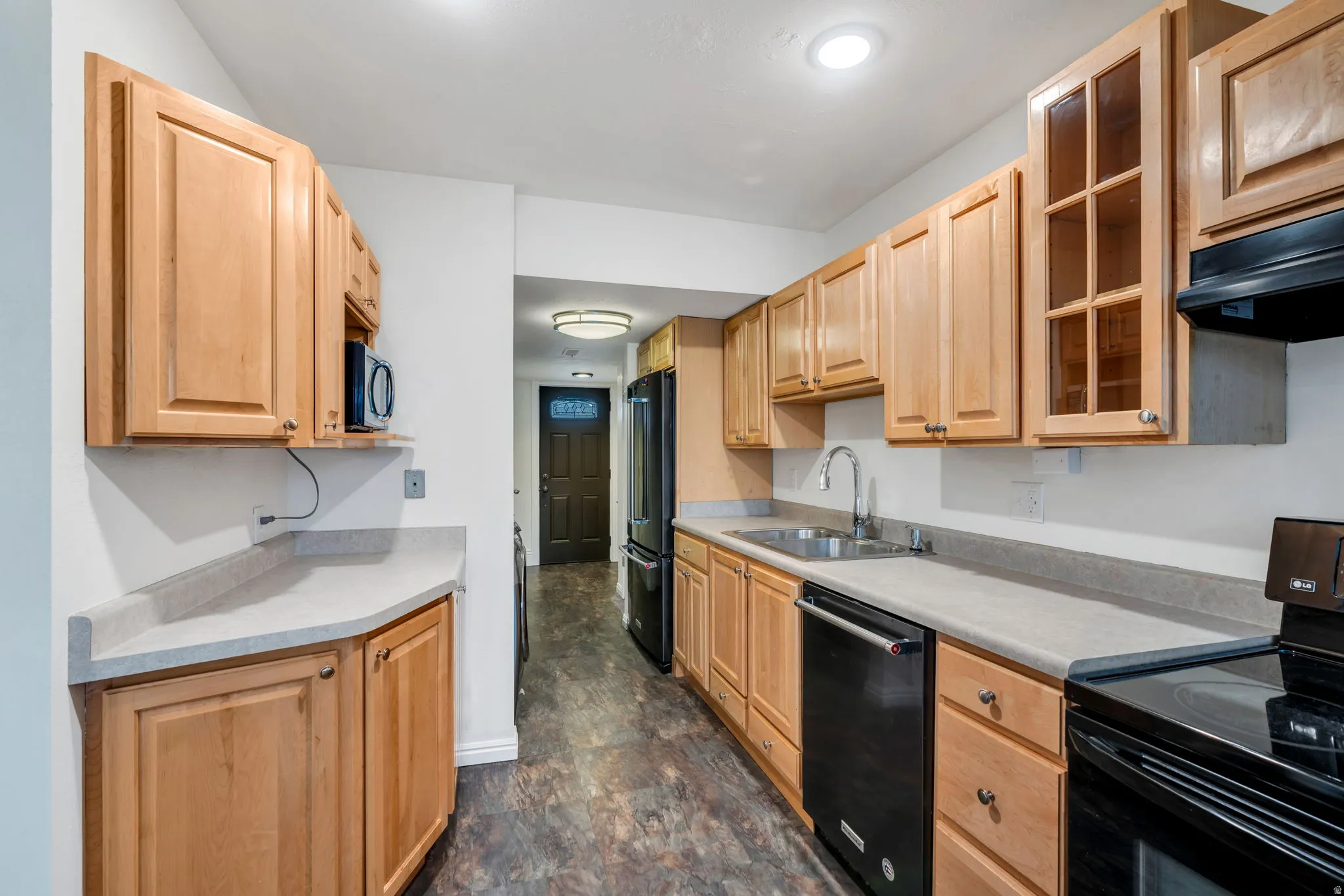 Kitchen featuring black appliances, glass insert cabinets, light countertops, light wood finish cabinets, and stone finish floors