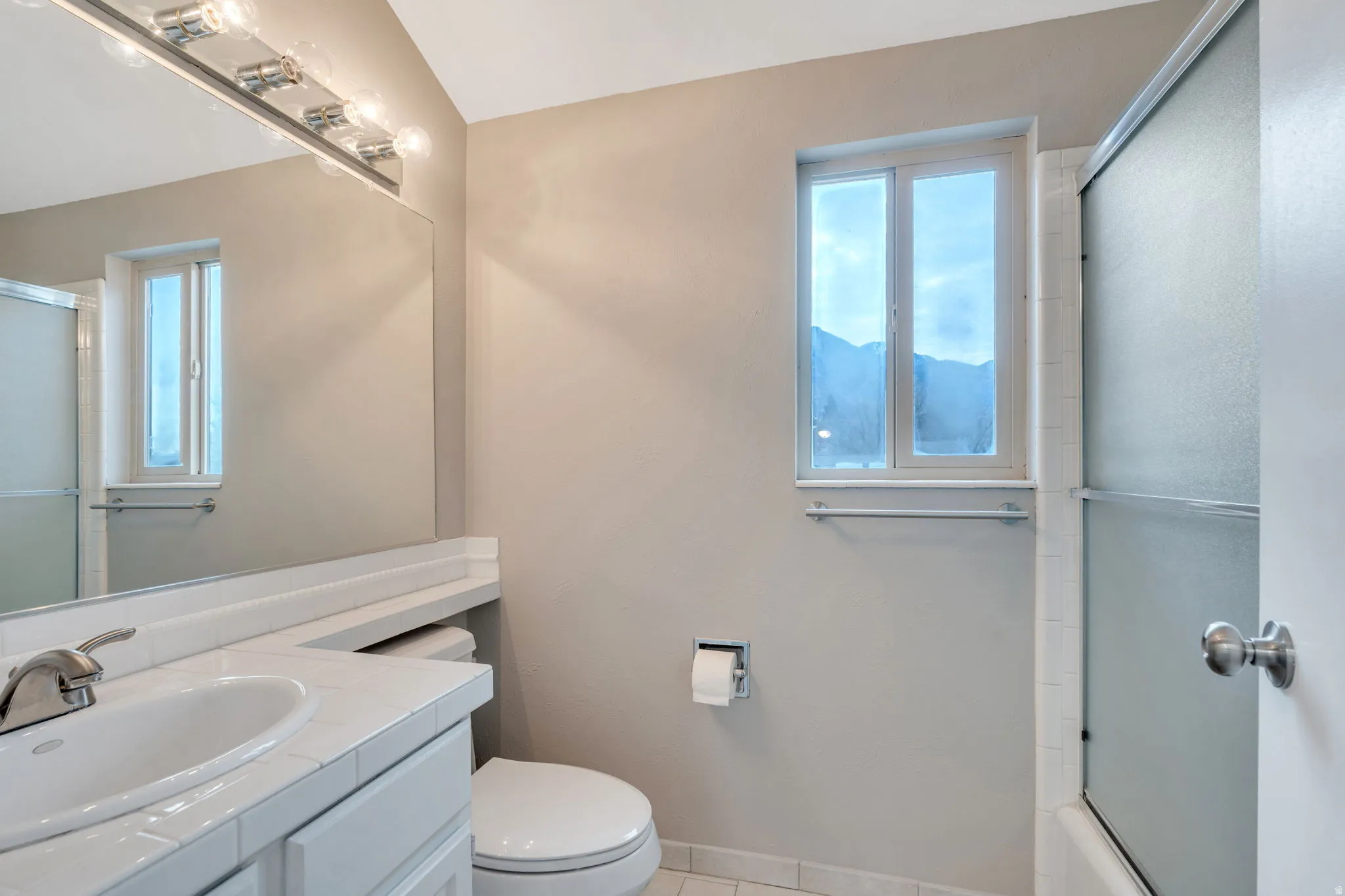 Bathroom featuring vanity, light tile patterned floors, plenty of natural light, and shower / bath combination with glass door