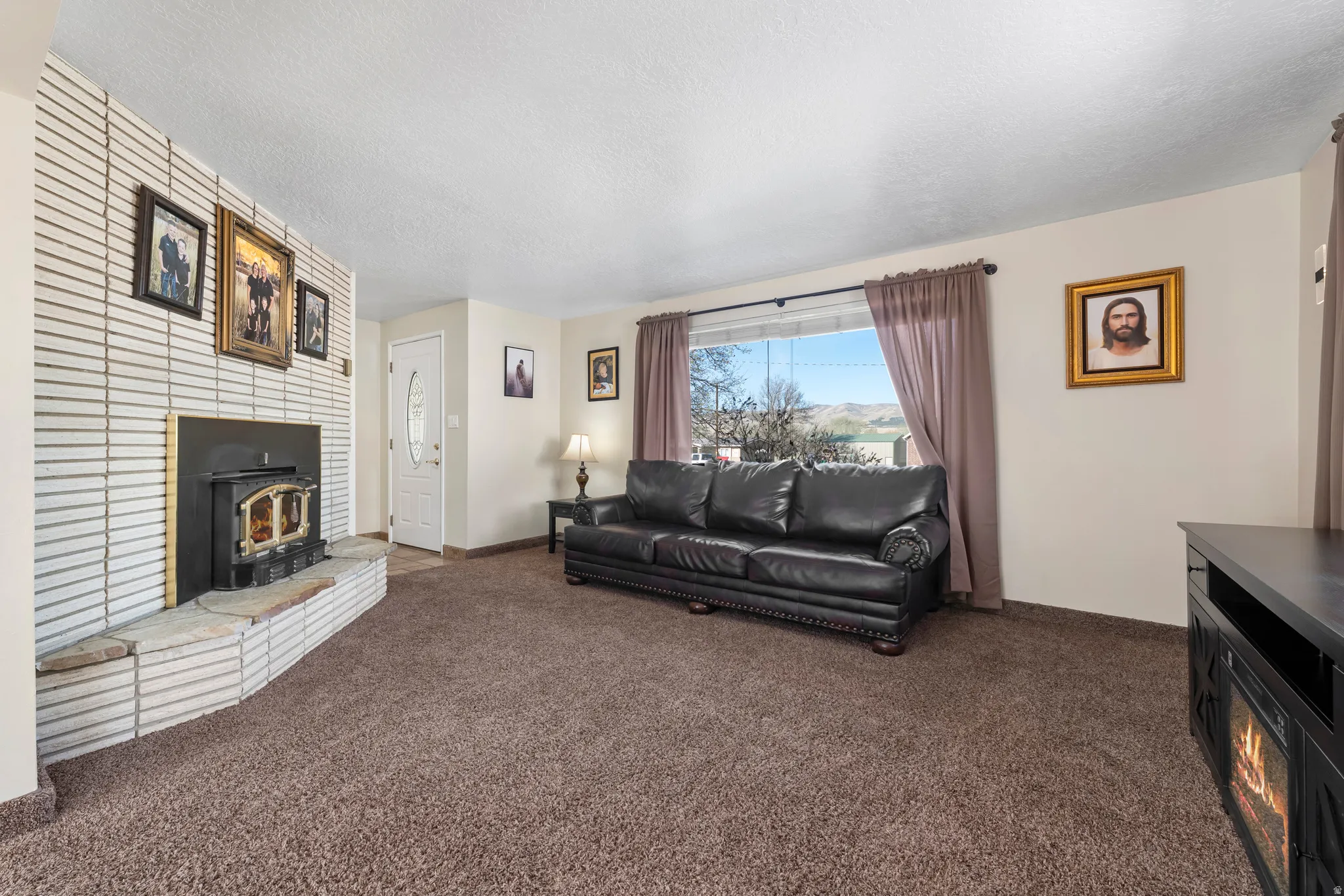 Living room with a wood stove, dark colored carpet, and a textured ceiling