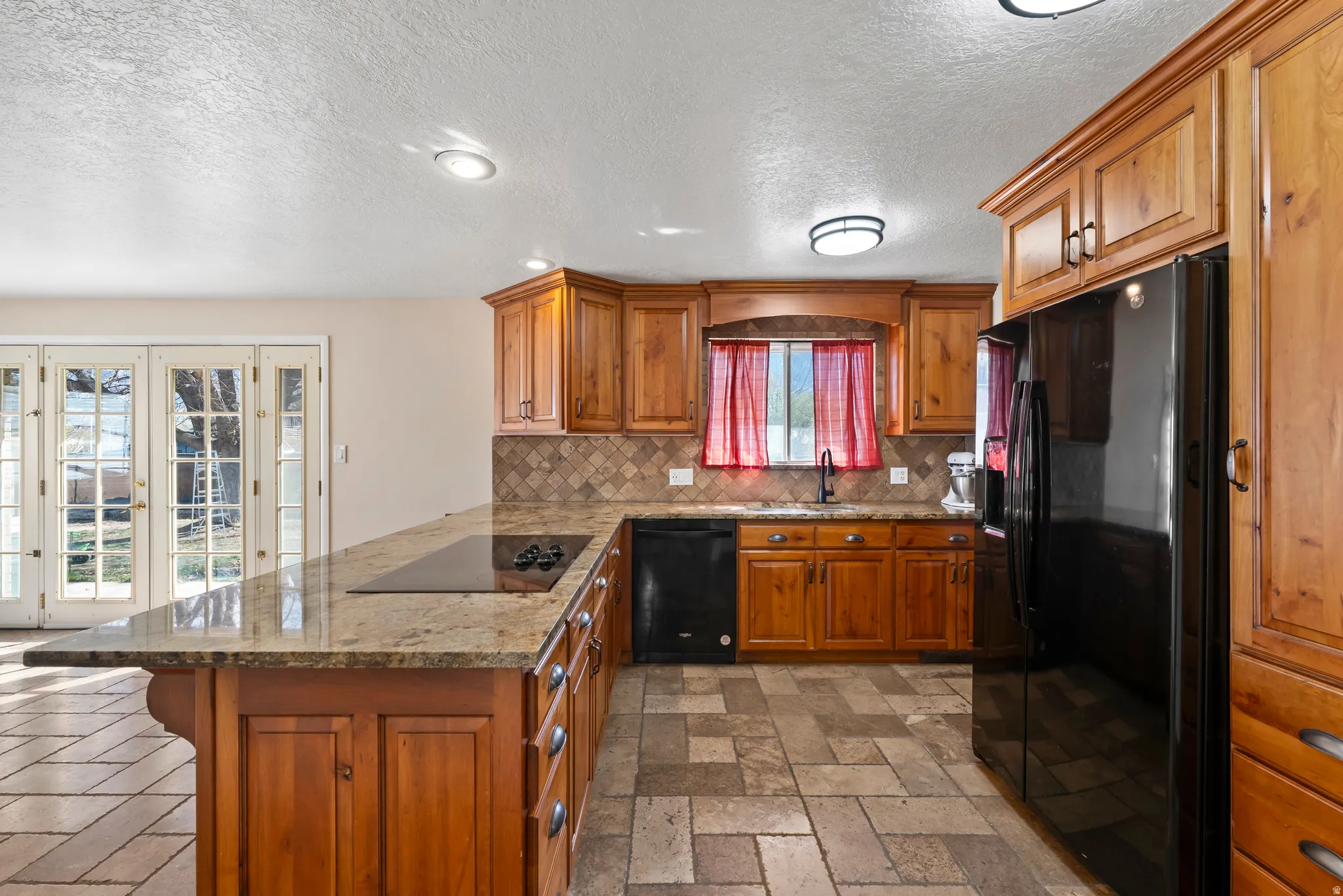 Kitchen with wood finish cabinets, black appliances, light stone countertops, a peninsula, and recessed lighting