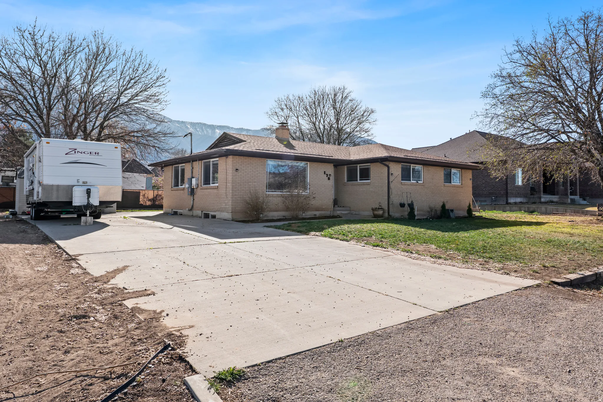Back of house with concrete driveway, brick siding, a lawn, and a chimney